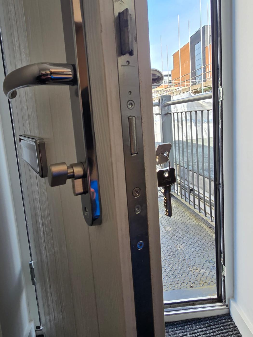 Composite door with a multi-point locking mechanism exposed during repair, replacement keys hanging from the cylinder.