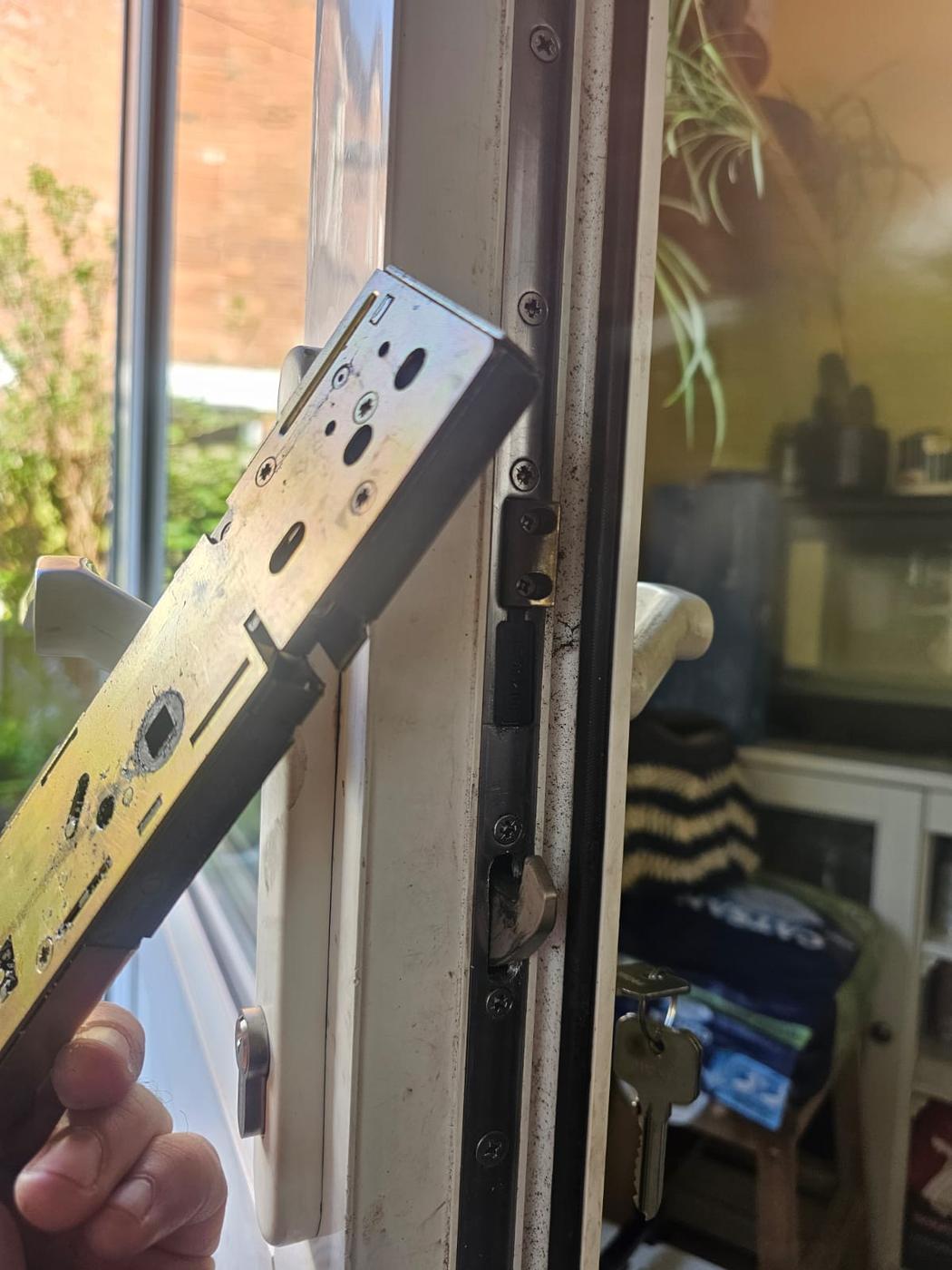 Broken uPVC gearbox held in a gloved hand next to the patio door it was removed from — failed mechanism diagnosed and replaced.