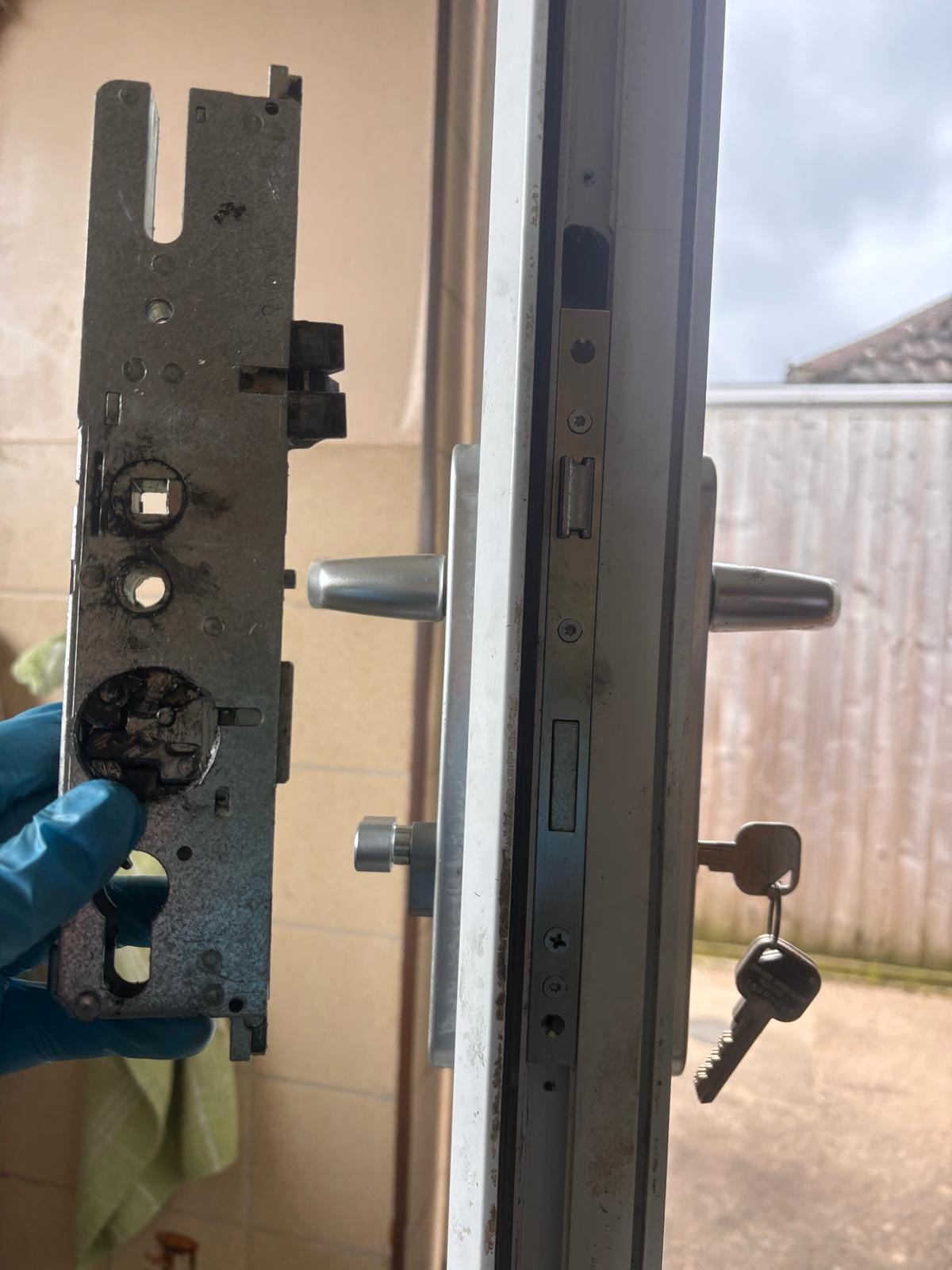 Faulty uPVC gearbox held in a blue-gloved hand for inspection — professional lock repair in progress.